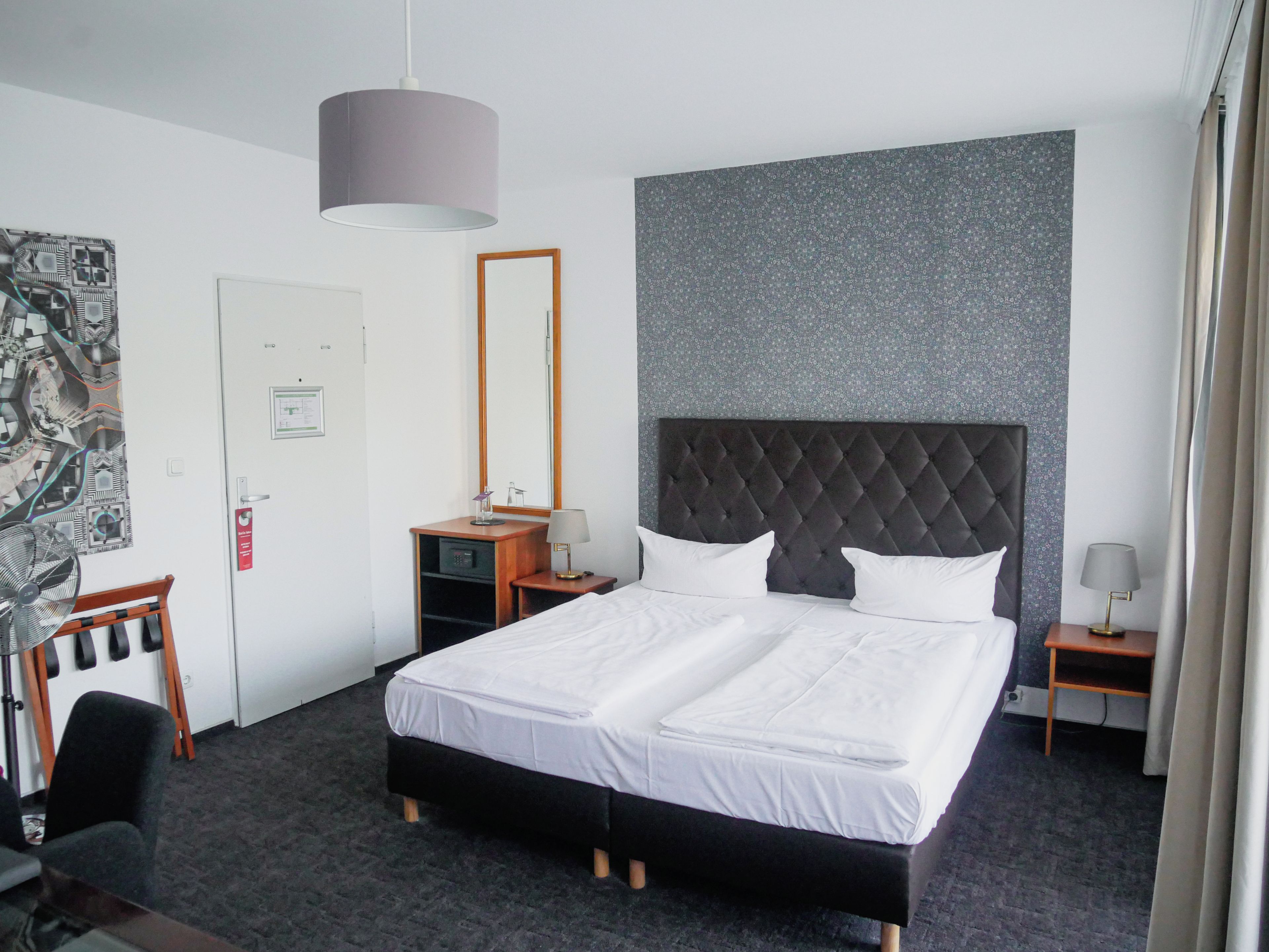 Een hotelkamer met een groot bed, een hoofdeinde, een bureau, een stoel, een bureaulamp, een staande lamp, een spiegel en een wand met een structuur.