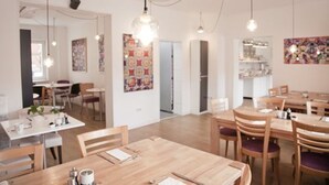 Un comedor moderno con mesas y sillas de madera, iluminación colgante y obras de arte en las paredes.