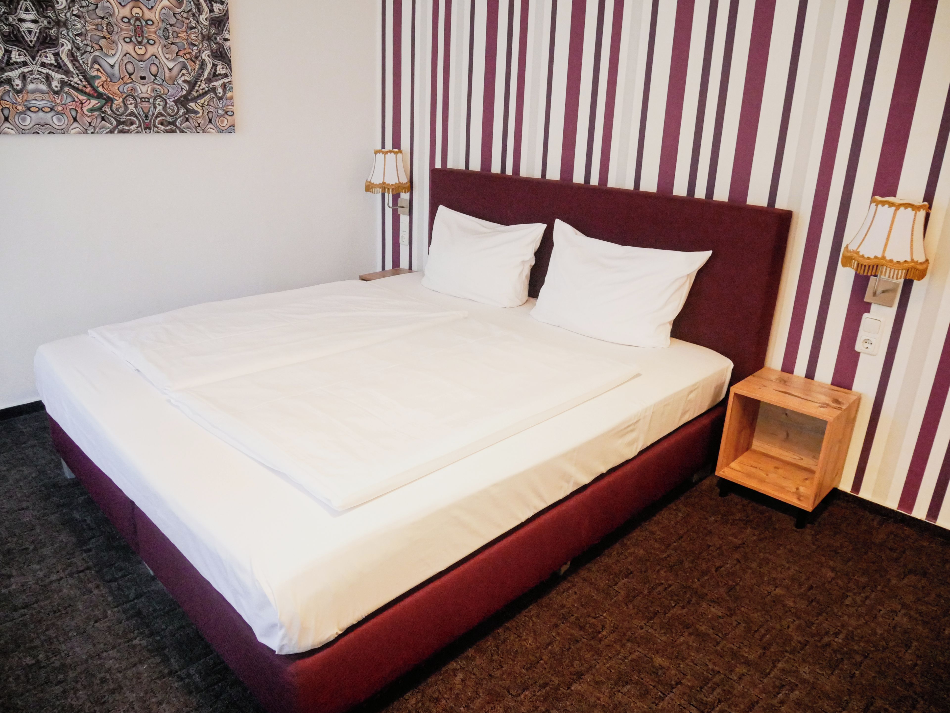 Ein ordentlich gemachtes Bett mit weißer Bettwäsche in einem Zimmer mit Streifen-Tapete und einem Nachttisch aus Holz.