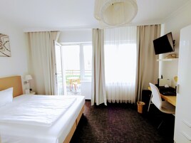 Una camera d'albergo con un letto grande, una scrivania con sedia, una televisione e un balcone con mobili da esterno.