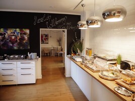 Zona de recepción de un hotel con diseño moderno, que incluye un mostrador de recepción, un cuadro colgado en la pared y un bufé con diferentes opciones de comida.