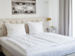 A neatly made bed with white linens, a tufted headboard, and a bedside table with a lamp.