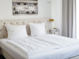 Un letto rifatto con lenzuola bianche, una testiera trapuntata e un comodino con una lampada.