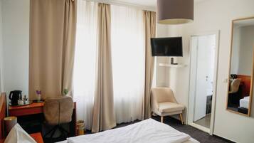 A hotel room with a bed, a desk with a chair, a television mounted on the wall, and a mirror.