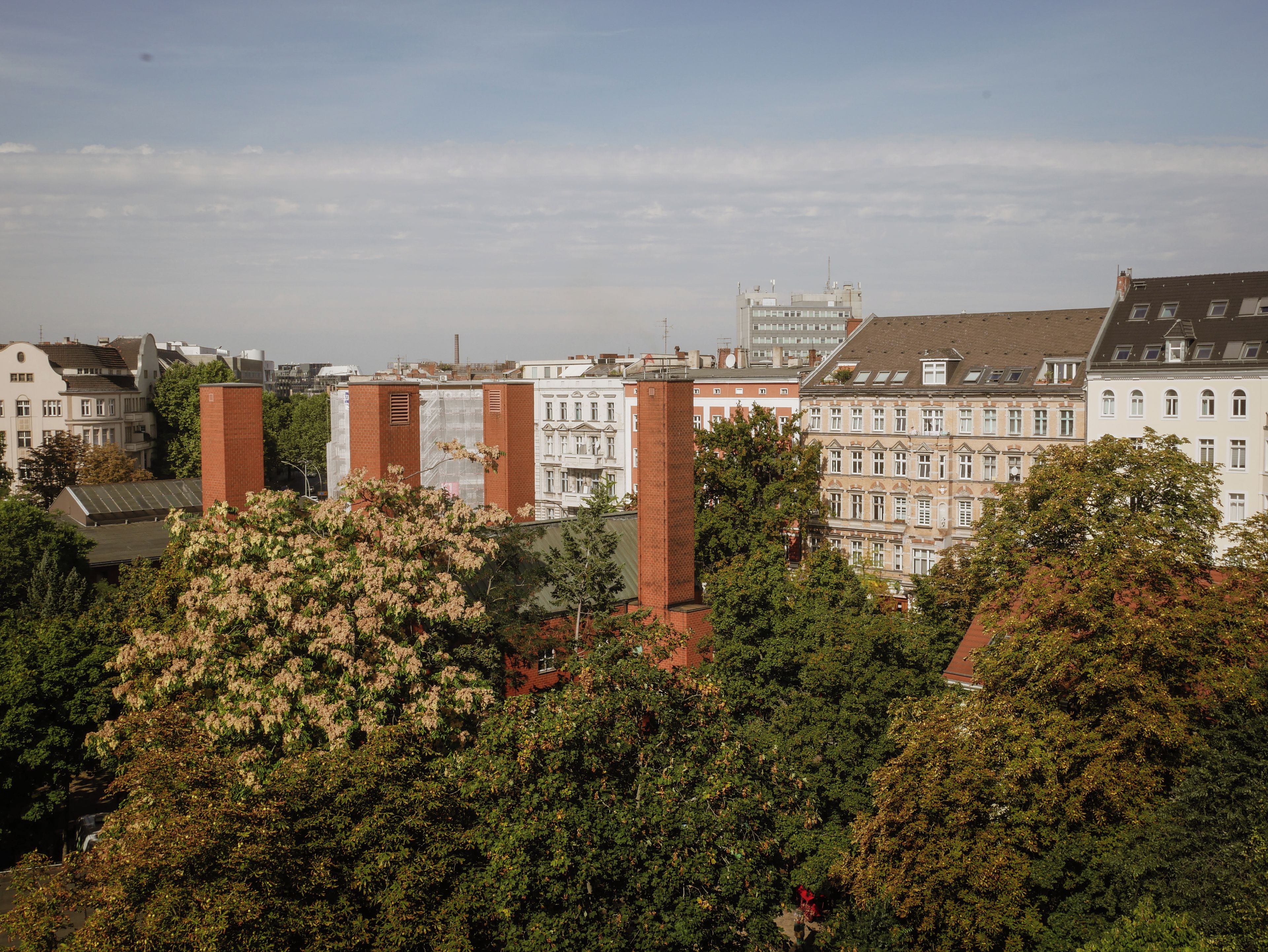 A cityscape with historic buildings, a prominent red brick structure, and lush green trees.