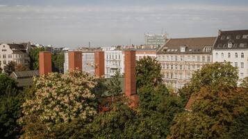 A cityscape with historic buildings, a prominent red brick structure, and lush green trees.