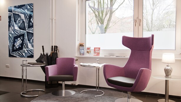 A modern room with two purple chairs, a small table, a rug, and a large abstract painting on the wall. - Hotel Les Nations (Berlin)
