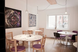 A dining area with round tables and chairs, a large abstract painting, and a window with a view of buildings.
