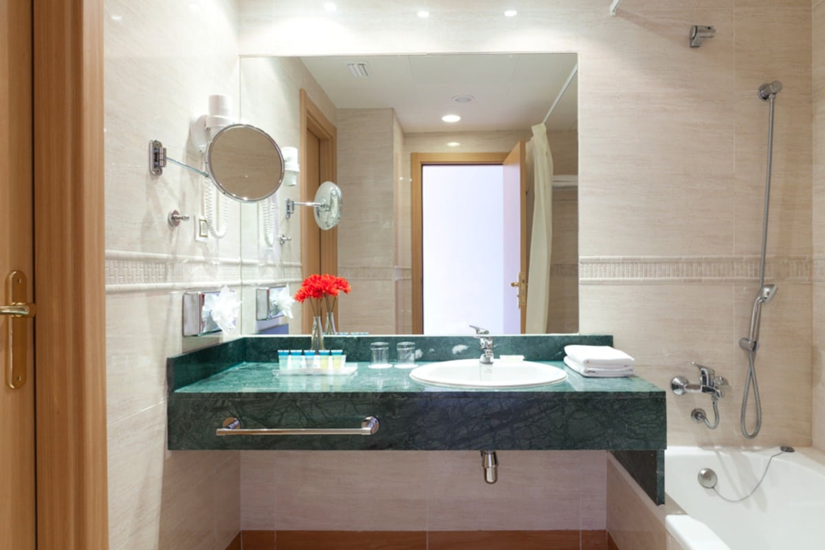 Une salle de bain moderne avec un comptoir en marbre, un lavabo, un miroir, une douche et un porte-serviettes.