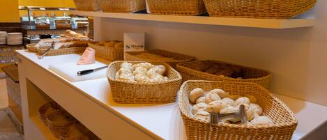 Zona de bufé con cestas de mimbre que contienen diversas opciones de panadería.