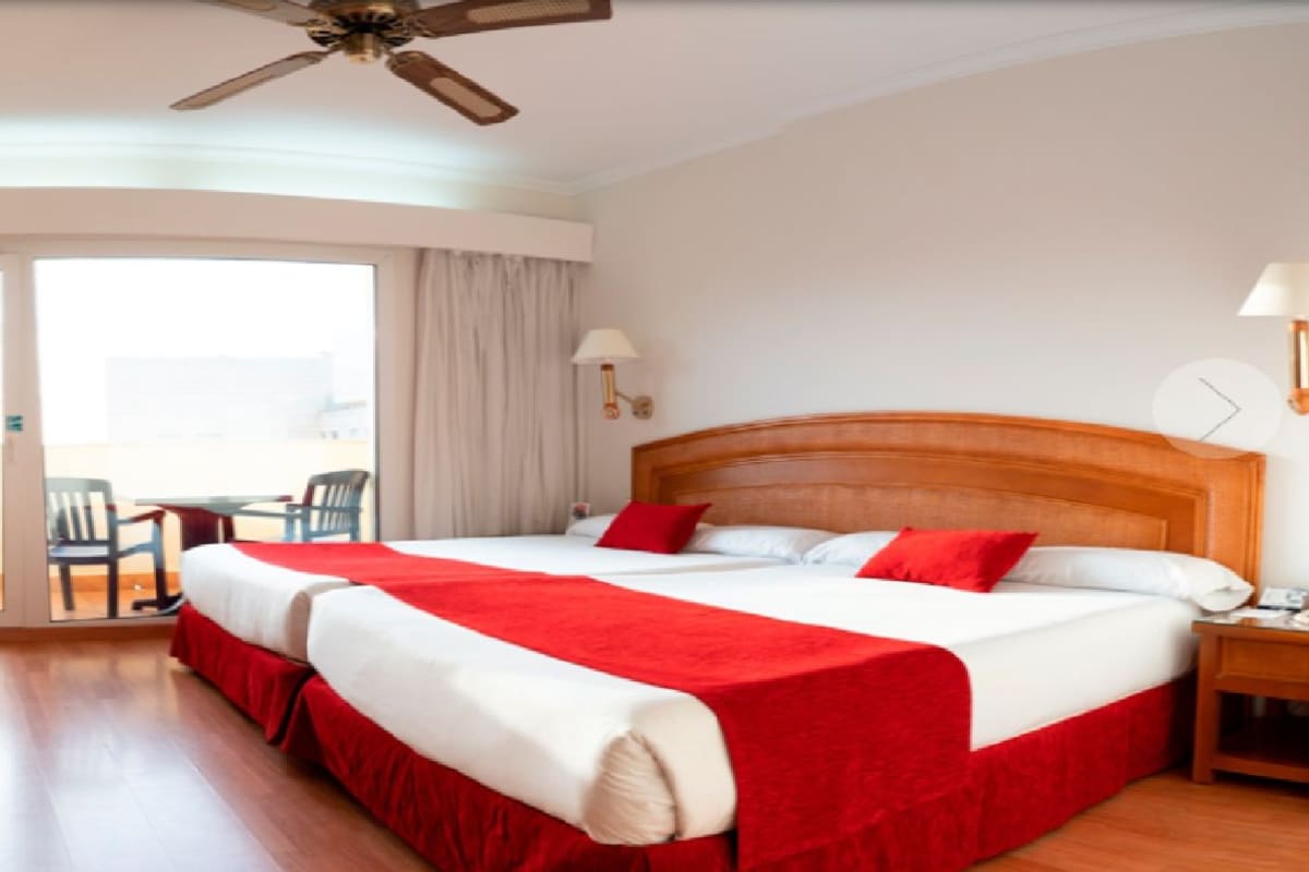 Une chambre d’hôtel avec un grand lit, un bureau, une chaise, une télévision et un balcon équipé de chaises.