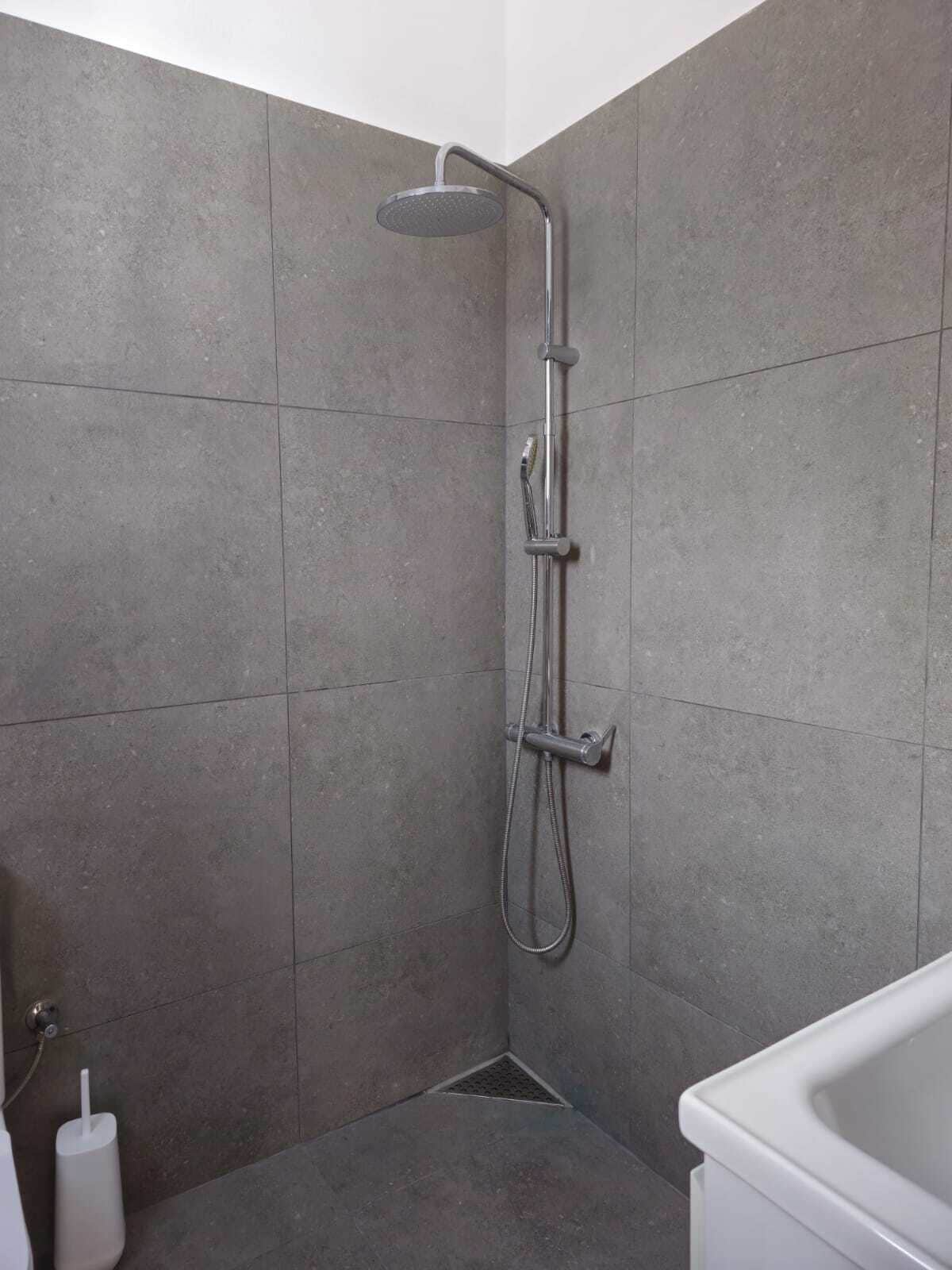 A modern shower with a handheld showerhead and a wall-mounted faucet.