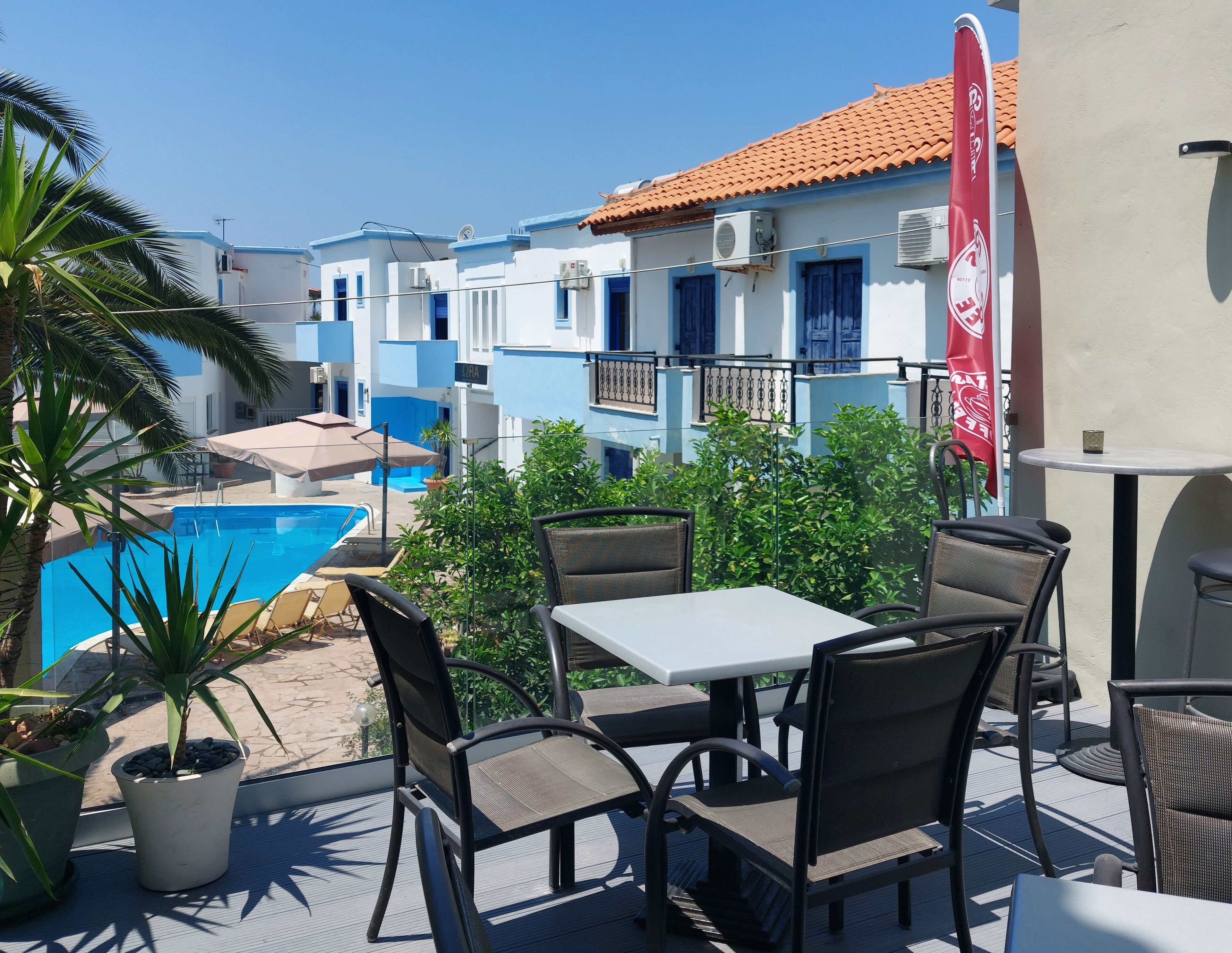 A poolside area with outdoor seating, a swimming pool, and buildings with blue and white facades in the background.