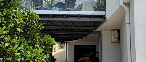 A covered outdoor area with a car parked inside a garage, potted plants, and a clear view of the street.