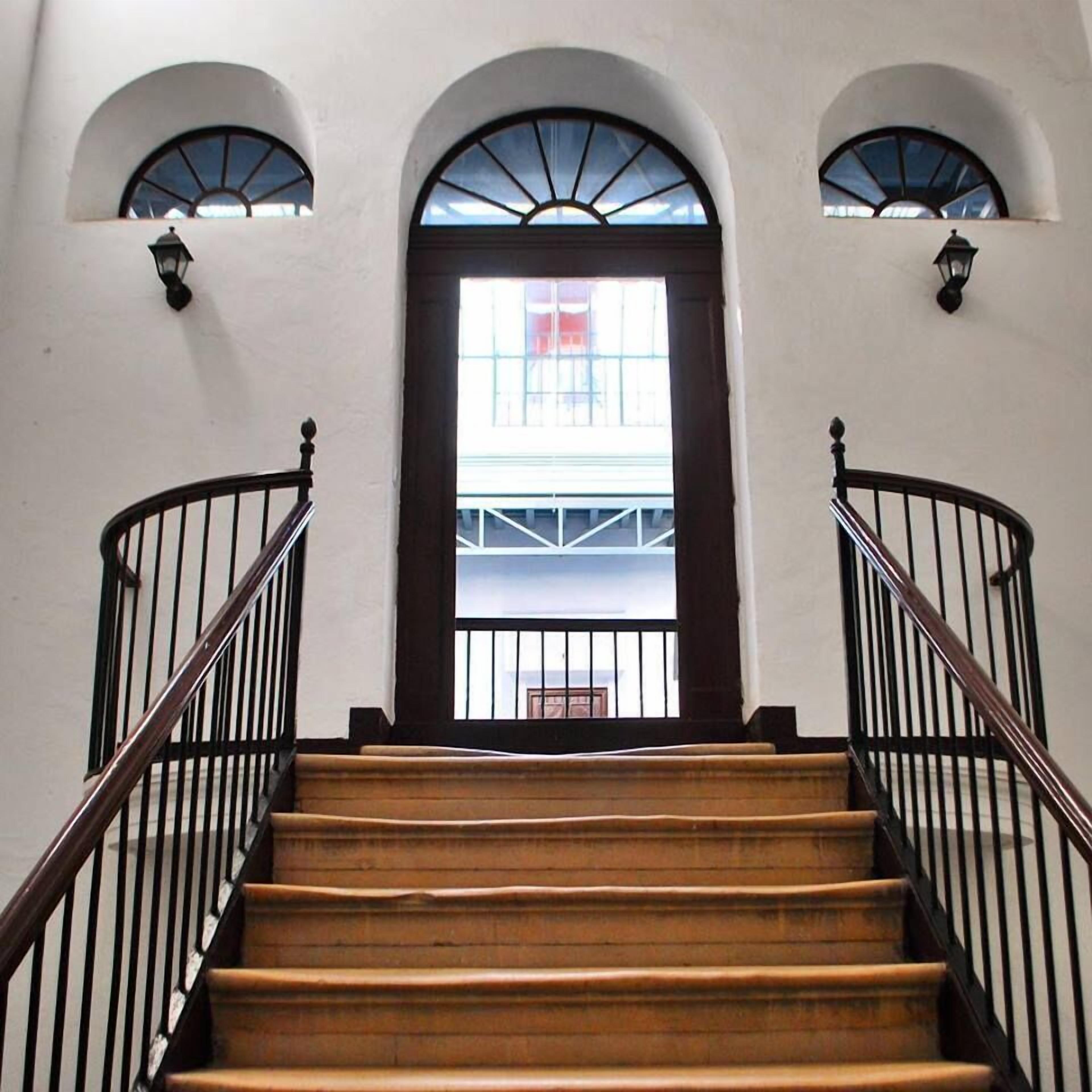 A staircase with wooden steps and black railings, leading to a door with a glass panel and a view of a building outside.