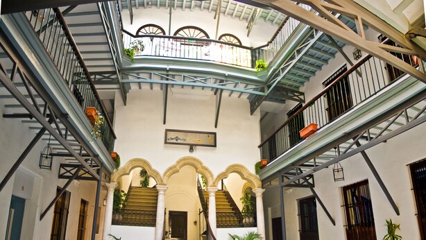 Un amplio atrio con piso a cuadros, múltiples escaleras y balcones con plantas en macetas.