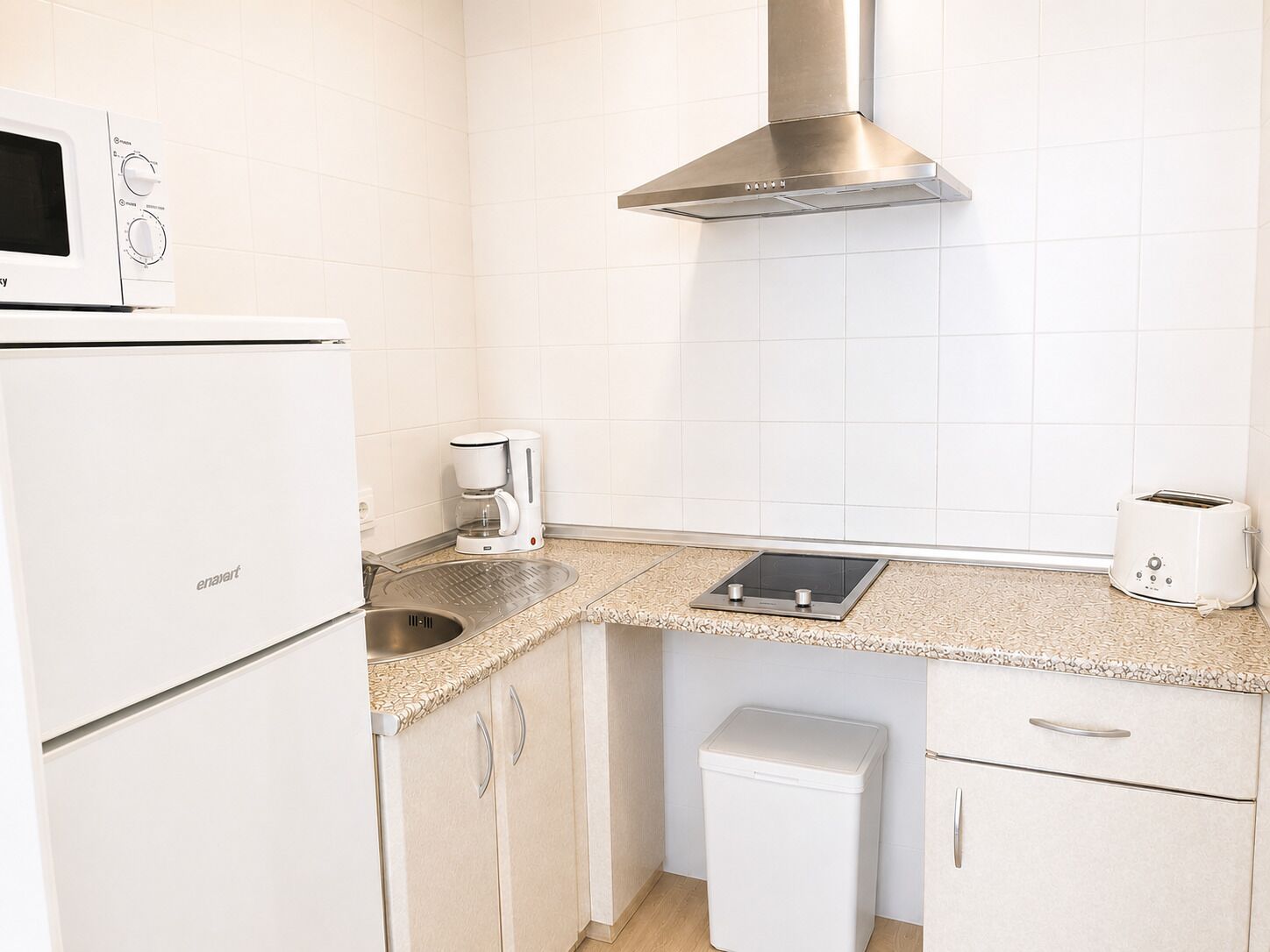 Una cucina compatta con forno a microonde, macchina del caffè, tostapane e un piccolo cestino.