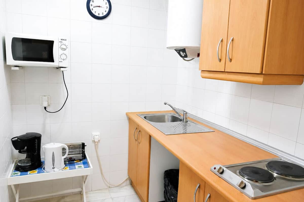 Een compacte keuken met een magnetron, spoelbak, fornuis en een klok aan de muur.