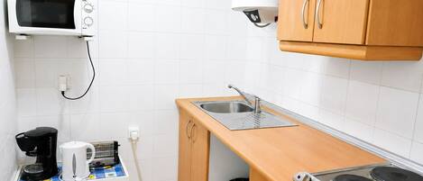 Una cocina compacta con microondas, fregadero, cocina y un reloj en la pared.