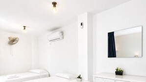 Habitación de hotel con dos camas, un tocador blanco, un espejo, un equipo de aire acondicionado y un ventilador de pared.