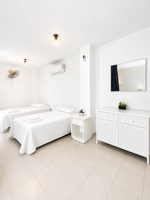 A hotel room with two beds, a white dresser, a mirror, an air conditioning unit, and a wall-mounted fan. - Apartamentos Larga 70 (El Puerto de Santa Maria)