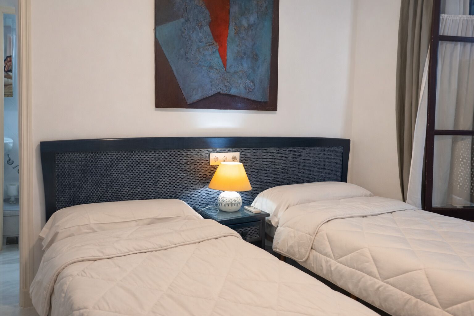 A hotel room with two beds, a nightstand with a lamp, and a painting on the wall.