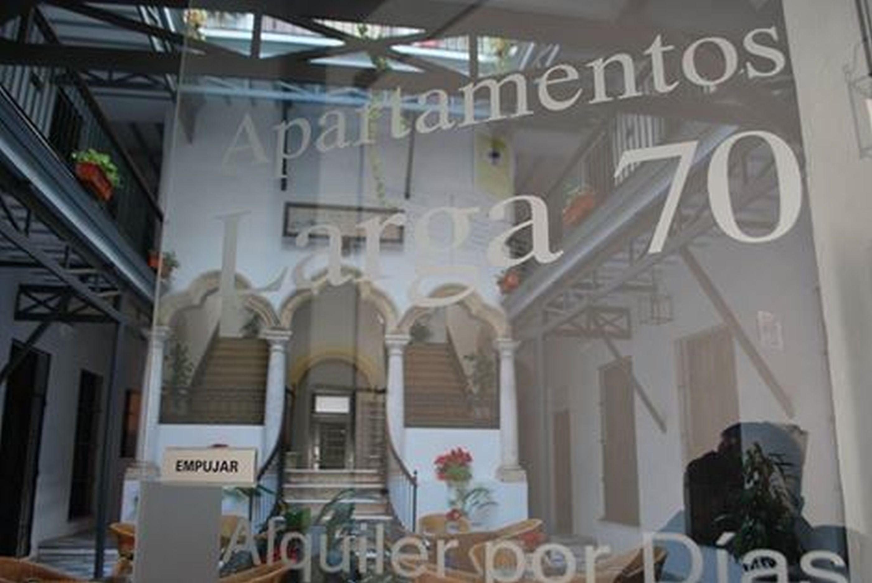 A hotel interior with a staircase, a sign reading "EMPUJAR", and a large window displaying "Apartamentos La 70".