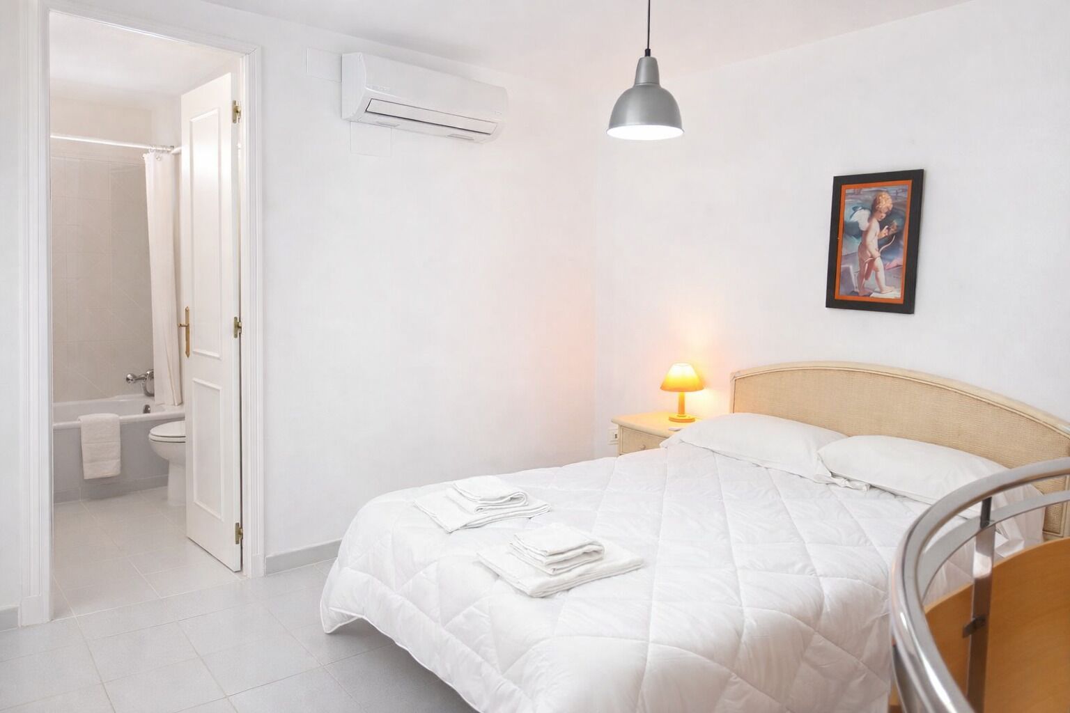 A bedroom with a bed, bedside lamp, and a picture on the wall.