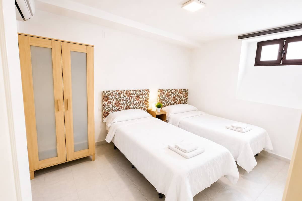 Een hotelkamer met twee bedden, een garderobe, een tafeltje met een plant en een raam.