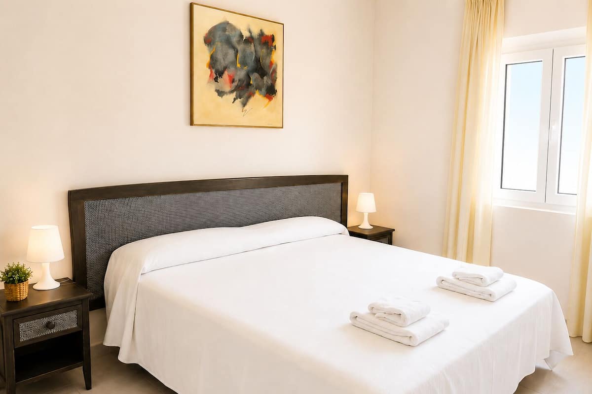 Een hotelkamer met een groot bed, twee nachtkastjes met lampen, een raam met gordijnen en een schilderij aan de muur.