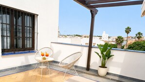 Una terraza en la azotea con una mesa, dos sillas, una planta en maceta y sillones de descanso.