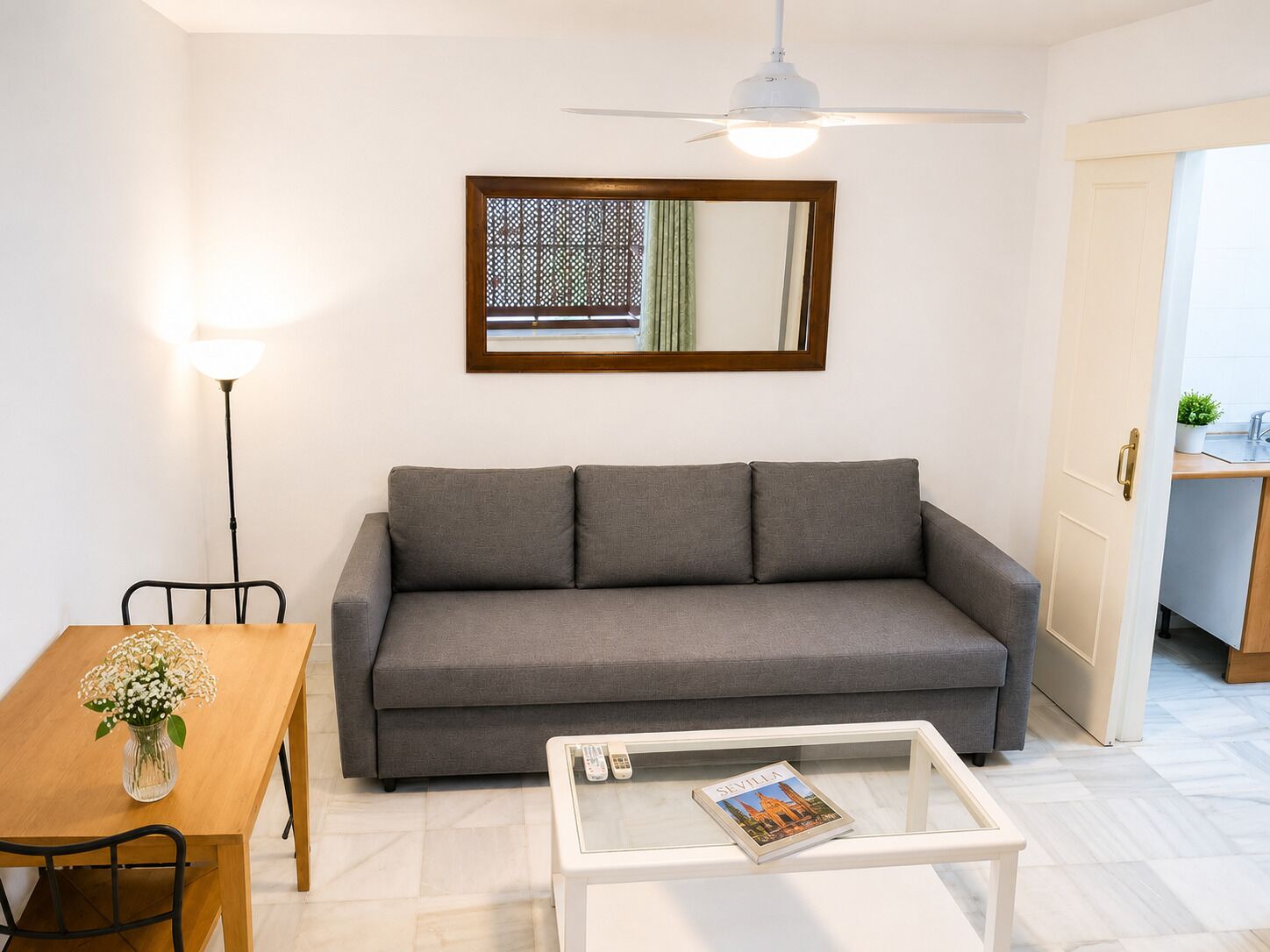 Un soggiorno con divano, tavolino, tavolo da pranzo con sedie, lampada e ventilatore a soffitto.
