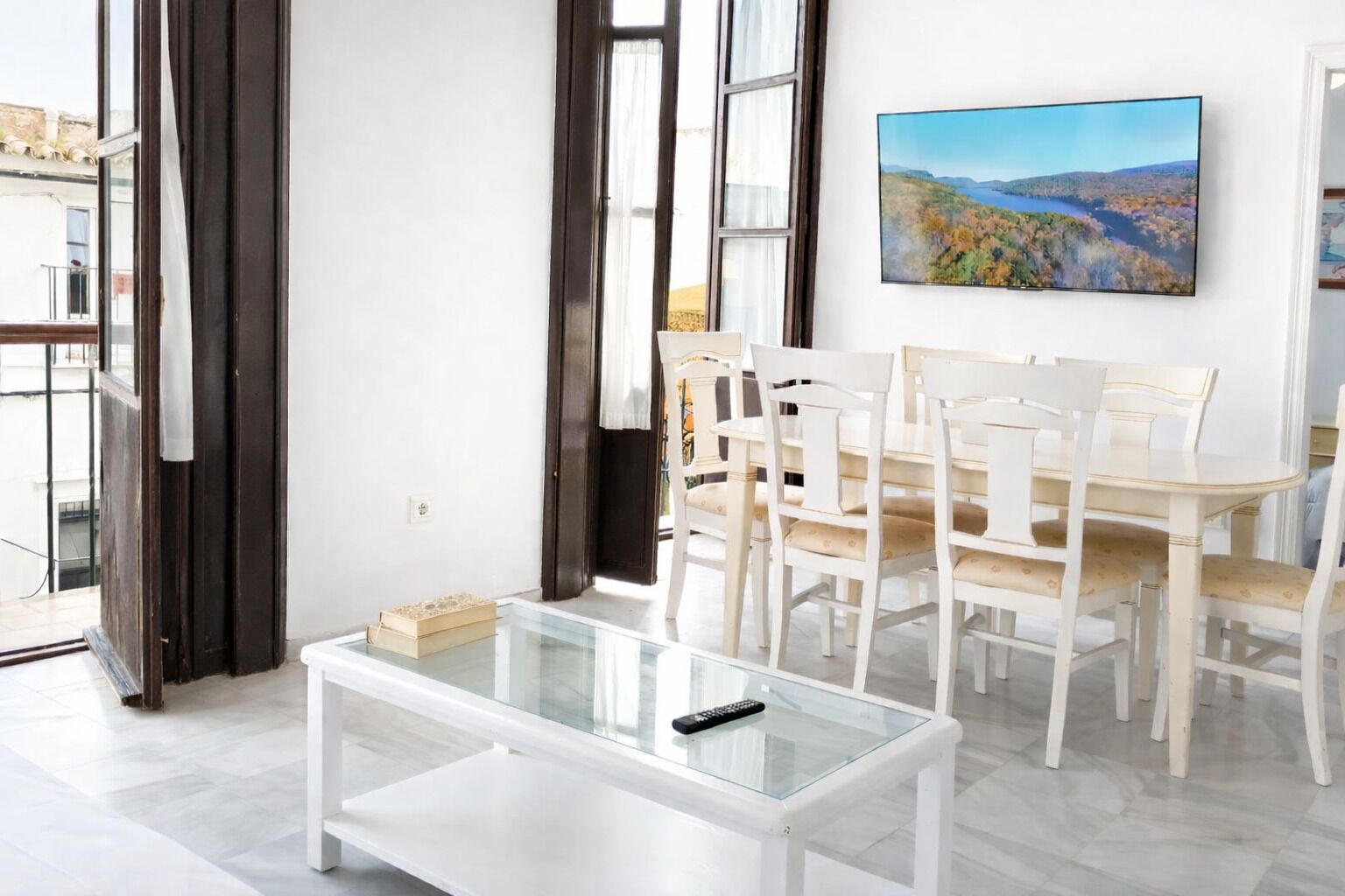 Una sala de estar moderna con una mesa de centro de vidrio, un comedor blanco y un cuadro en la pared.