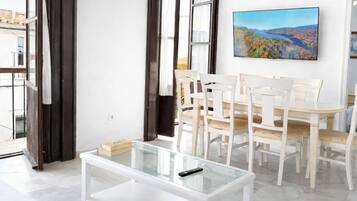 Una sala de estar moderna con una mesa de centro de vidrio, un comedor blanco y un cuadro en la pared.