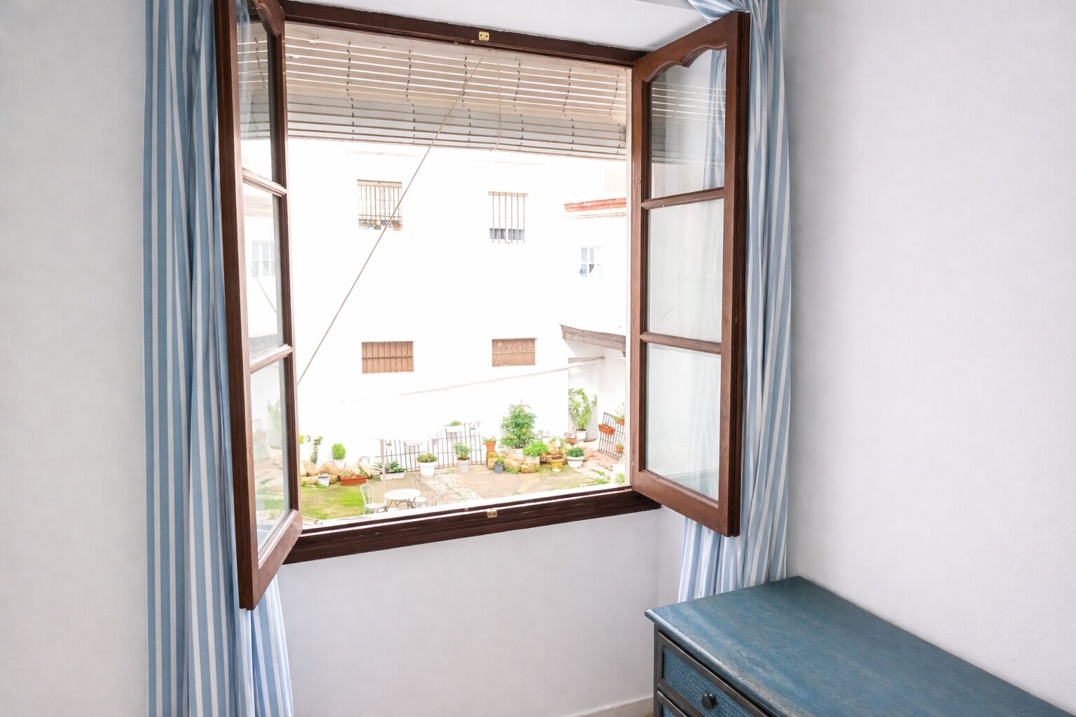 A room with a window overlooking a courtyard with potted plants and a building in the background.