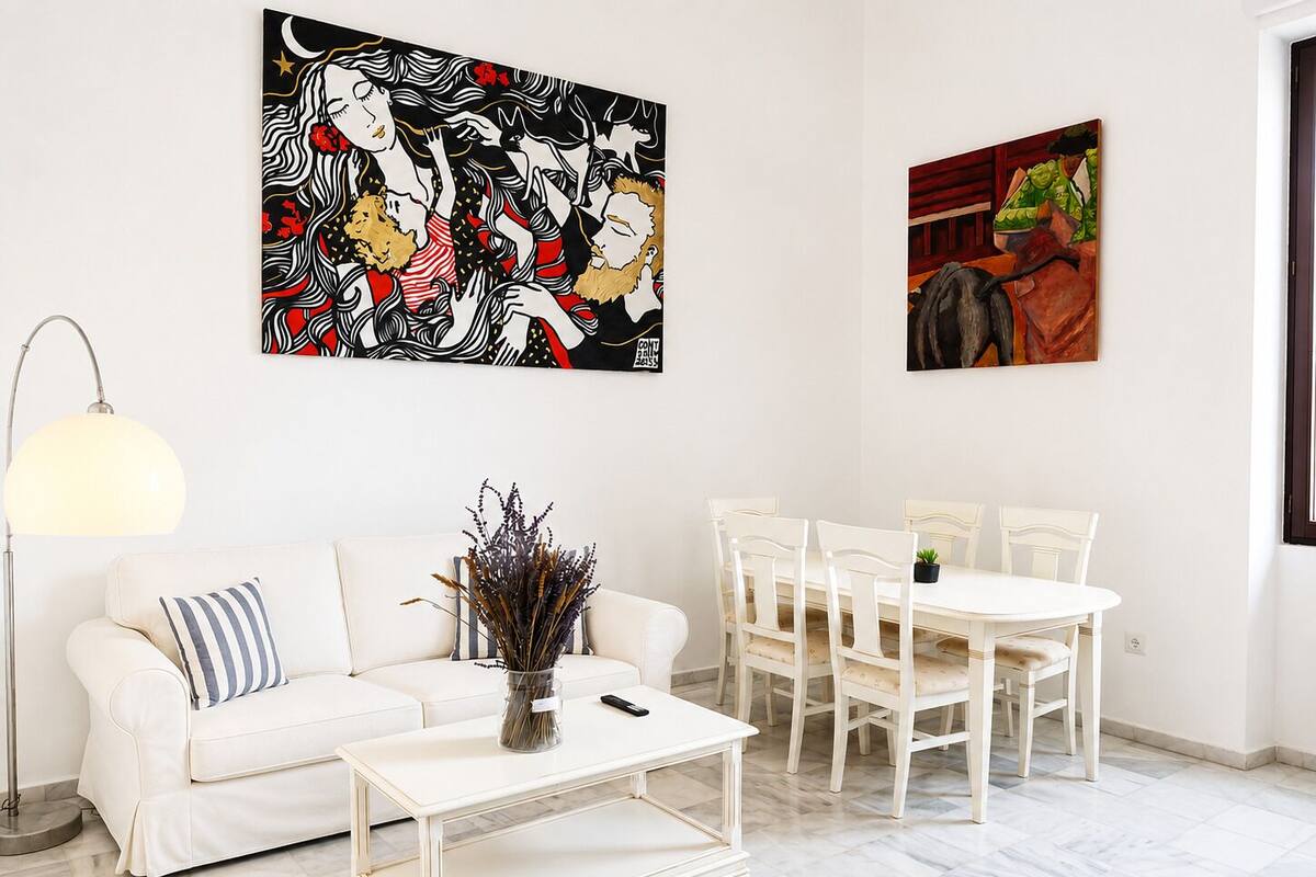 Een woonkamer met een witte bank, een salontafel, een eettafel met stoelen en twee kunstwerken aan de wand.