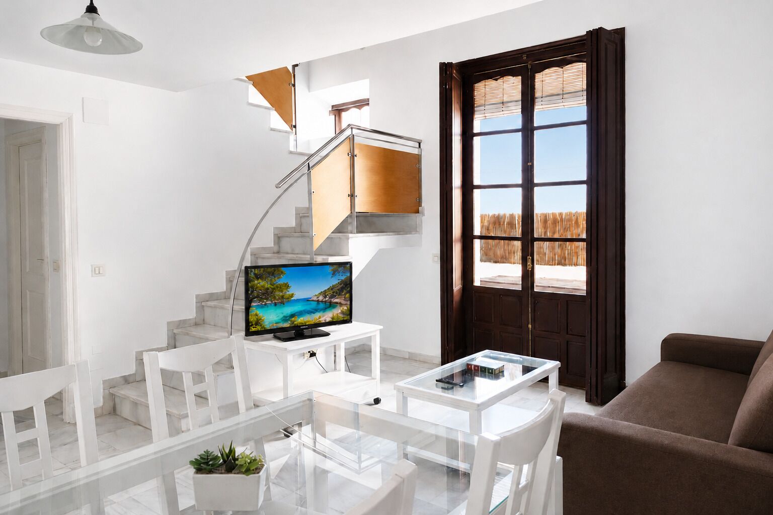 Un salon moderne avec un escalier blanc, un téléviseur, une table basse en verre et un canapé marron.