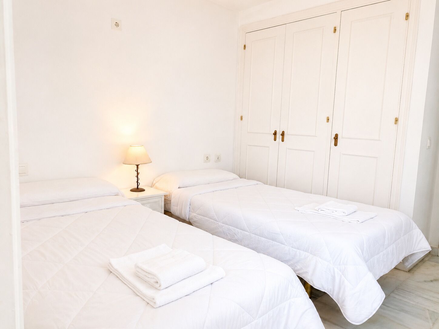 Een hotelkamer met twee enkele bedden, een nachtkastje met een lamp en een grote witte inbouwkast.