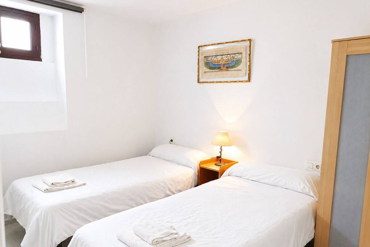 Een hotelkamer met twee eenpersoonsbedden, een nachtkastje met lamp, een lijst met afbeelding aan de muur en een raam.