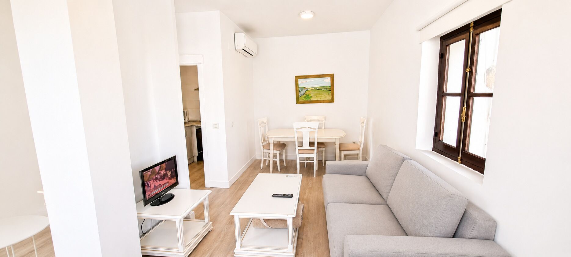 A compact living space with a sofa, a dining table with chairs, a TV, and a window with a view.