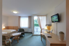 Hotellihuone, jossa on sänky, työpöytä tuolilla, televisio ja ikkuna, jossa on verhot.