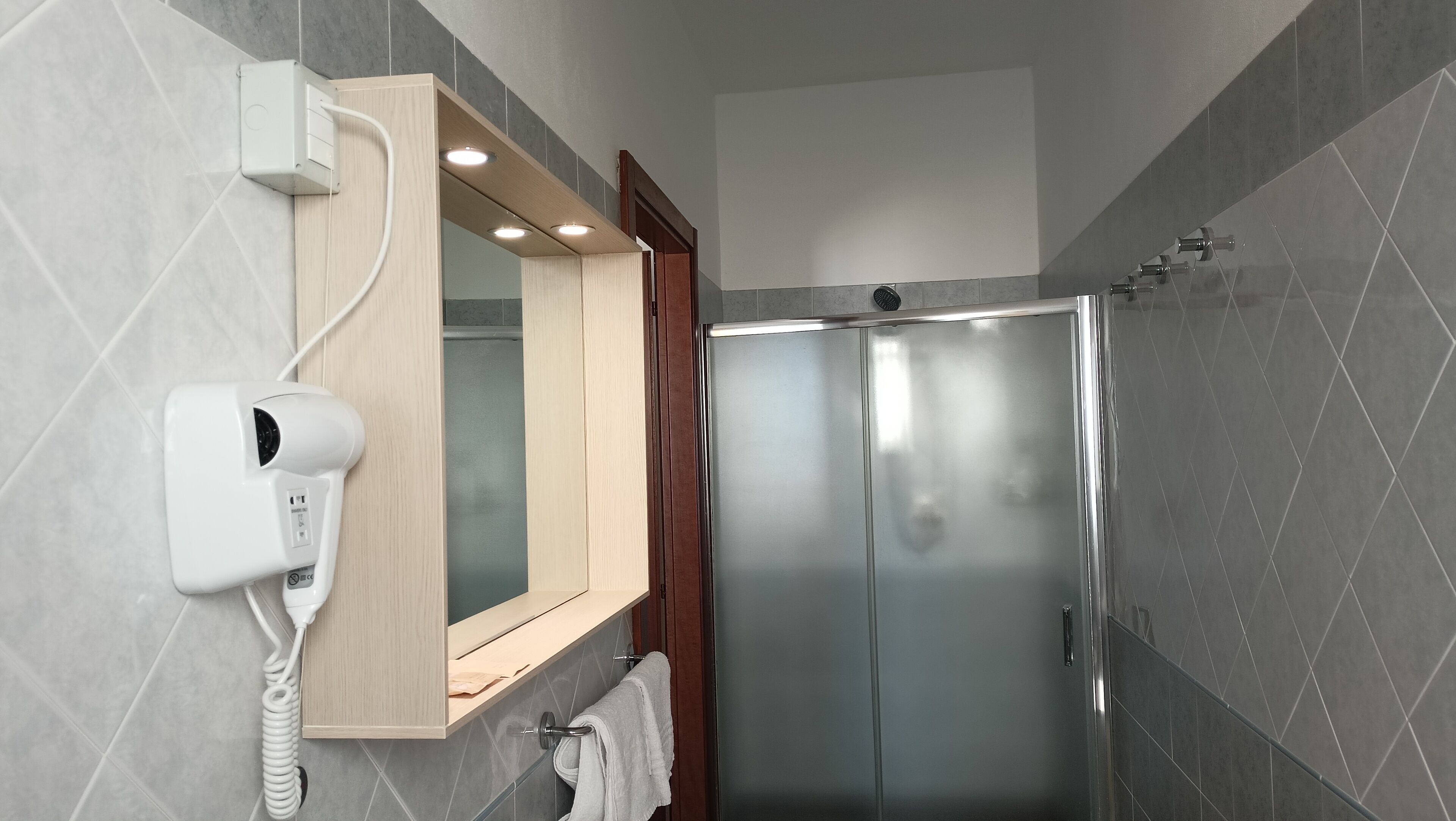 A modern bathroom with a built-in hairdryer, a mirror, and a walk-in shower.