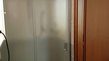 Un baño con cabina de ducha de vidrio, lavamanos blanco y puerta de madera.