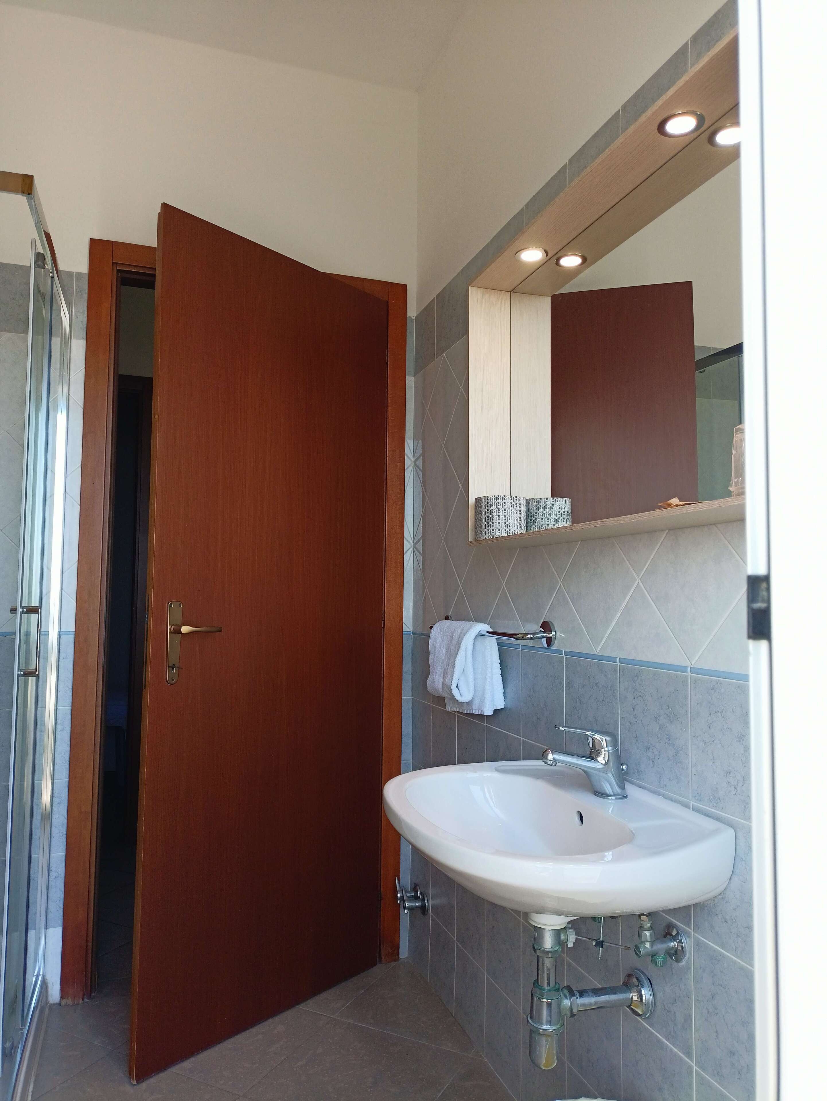 Un baño con puerta de madera, un lavabo blanco, un espejo y paredes con azulejos.