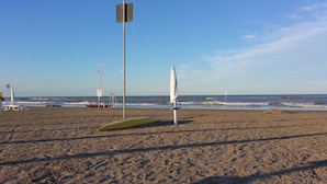 Een strand met een redershut, een rode redderboot en een geel surfboard.