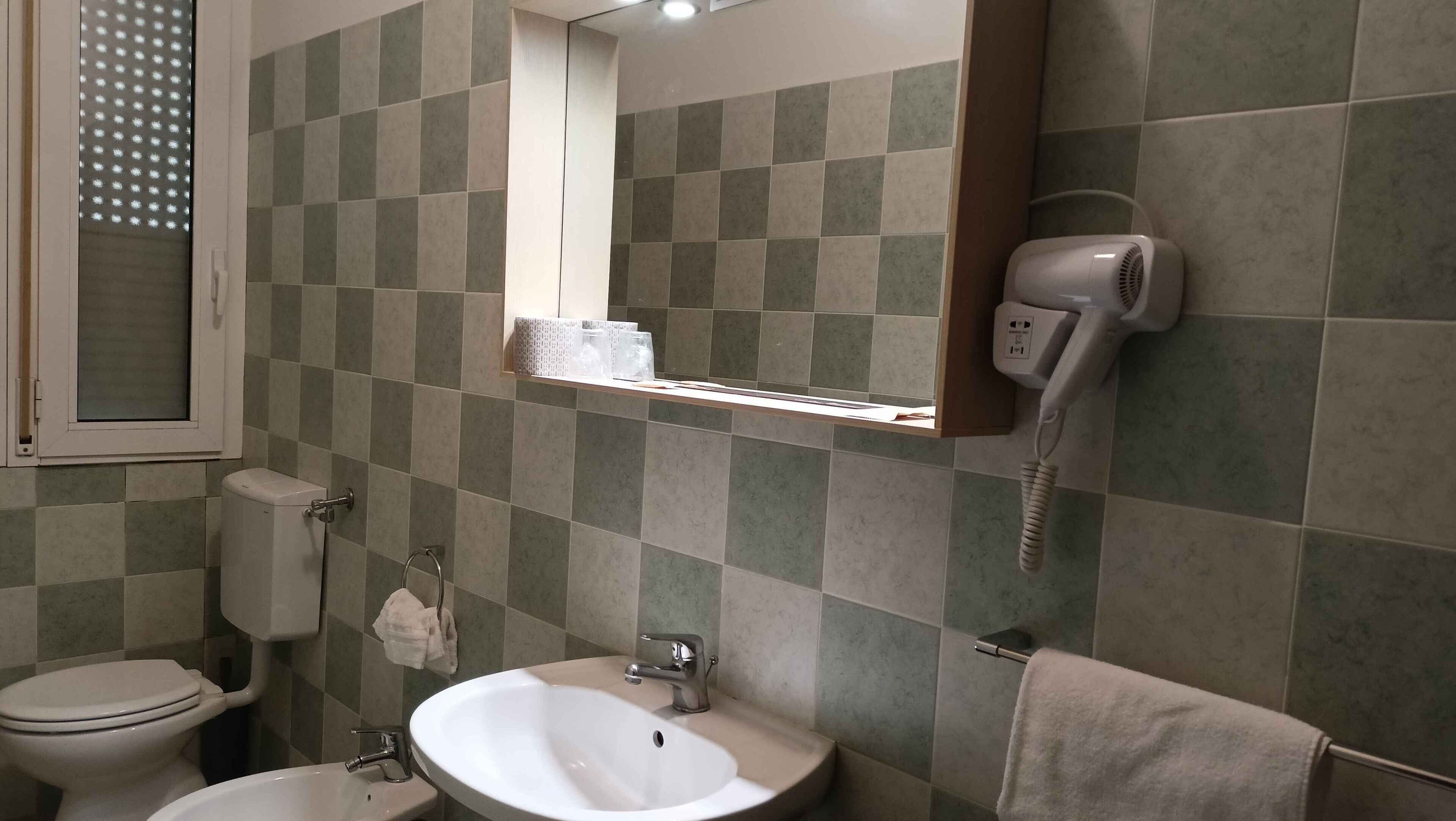 Une salle de bain équipée de toilettes, d’un lavabo et d’un sèche-cheveux fixé au mur.