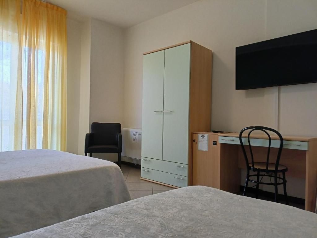 Habitación de hotel con dos camas, un escritorio, una silla, un armario y un televisor.