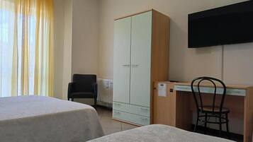 Habitación de hotel con dos camas, un escritorio, una silla, un armario y un televisor.