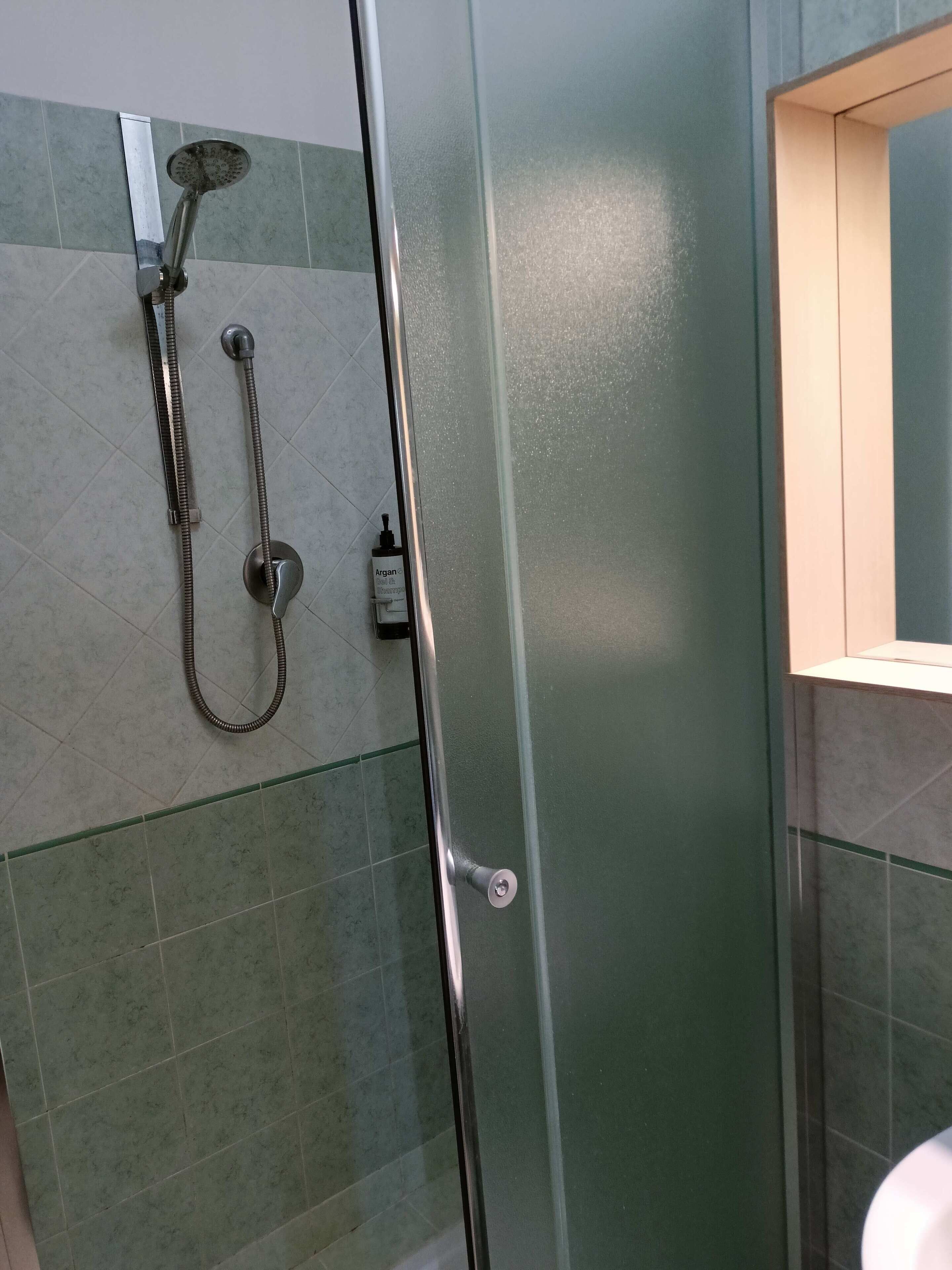 A glass-enclosed shower with a handheld showerhead and a wall-mounted faucet.