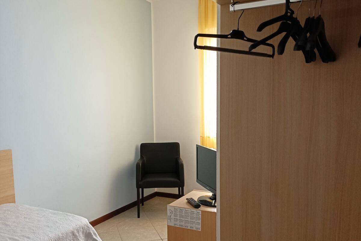 A hotel room with a bed, a desk with a computer, a chair, and a coat rack.